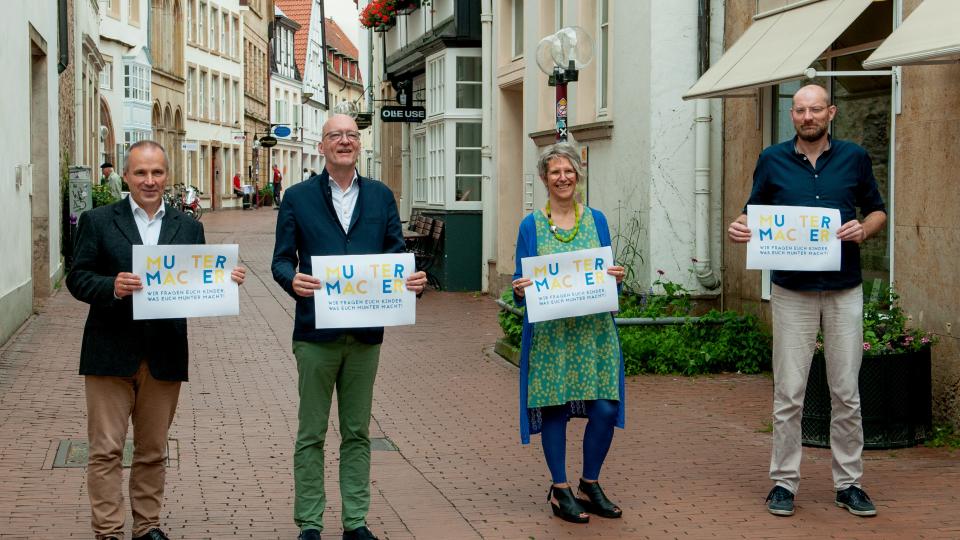 4 Personen in einer Straßenflucht in der Stadt OS mit Logoplakaten in der Hand
