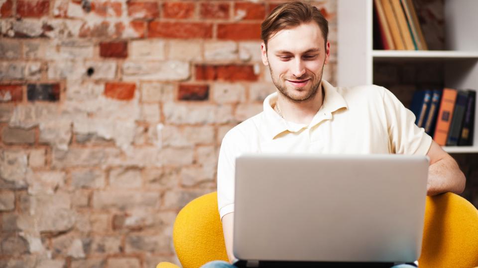 Ein Mann, der mit einem Laptop auf dem Schoß in einem Sitzsack sitzt und auf den Bildschirm schaut.
