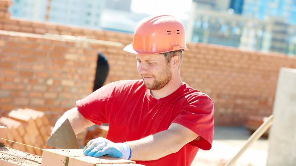 Ein junger Mann mit Sicherheitshelm arbeitet auf einer Baustelle.