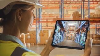 Eine Frau hält ein Tablet in der Hand und schaut dadurch in einen Lagerraum